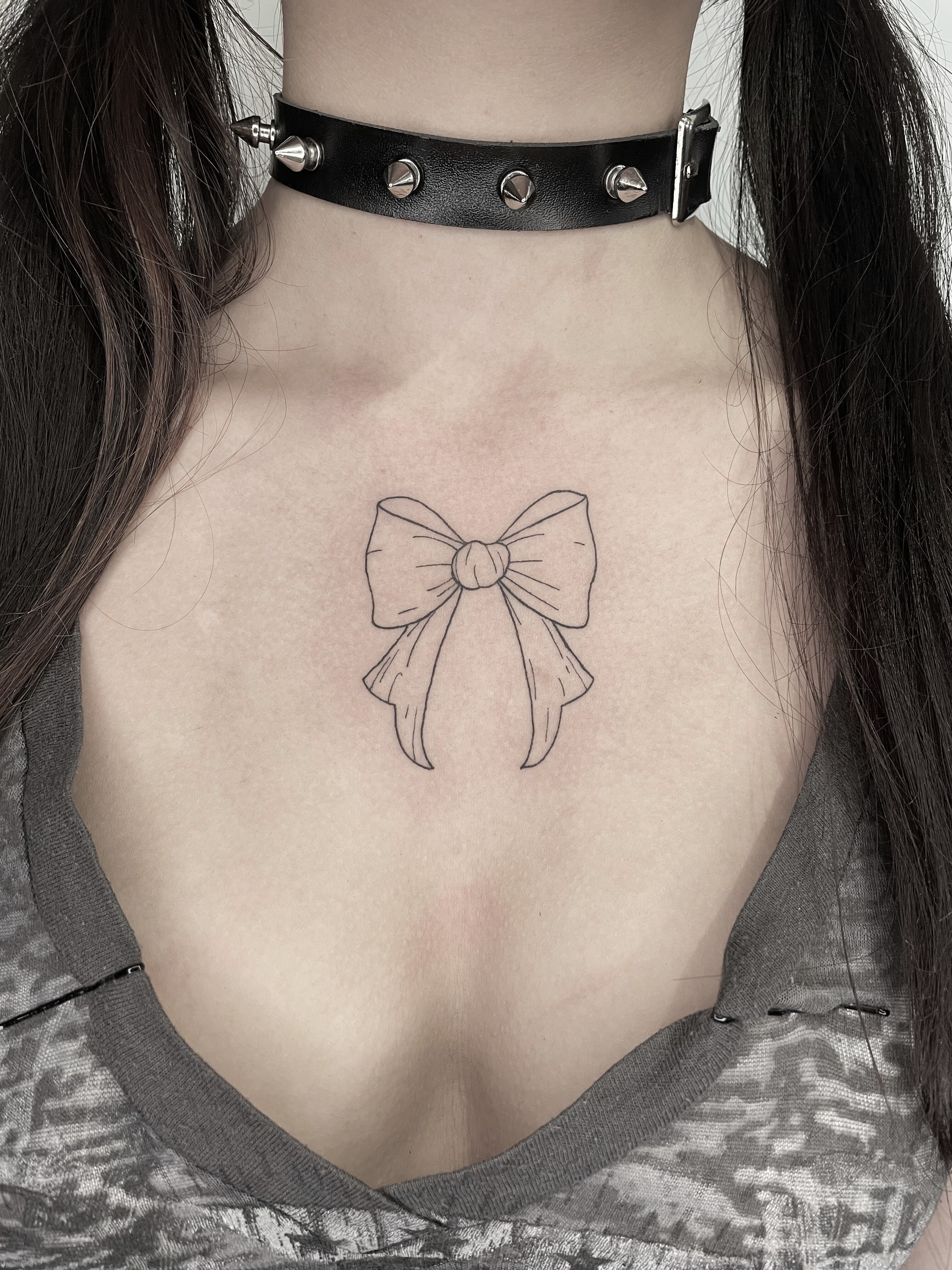 minimalist fine line bow tattoo on the chest