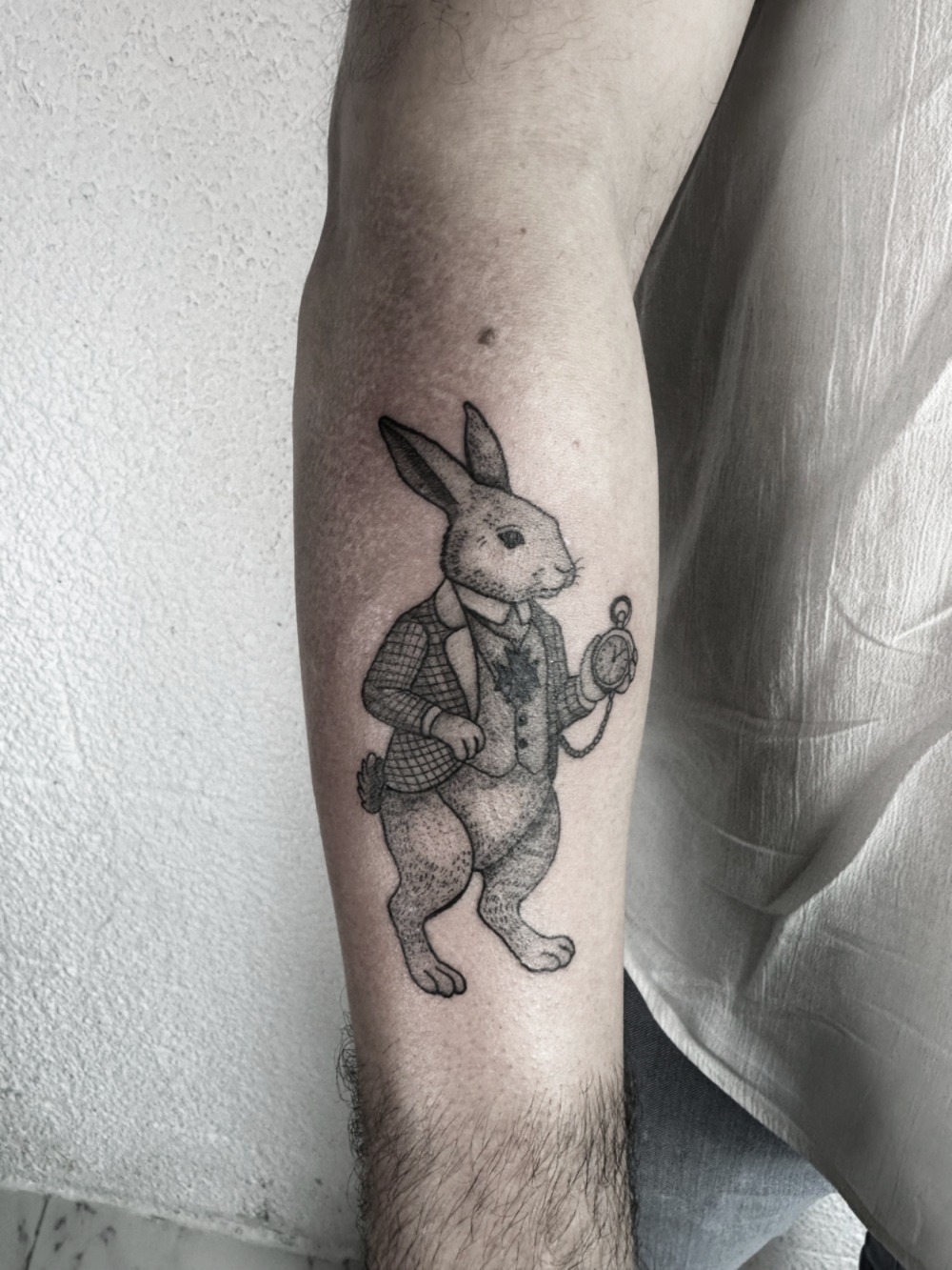Illustrative black ink tattoo of a rabbit holding a pocket watch, fine line and dotwork tattoo style, whimsical animal tattoo