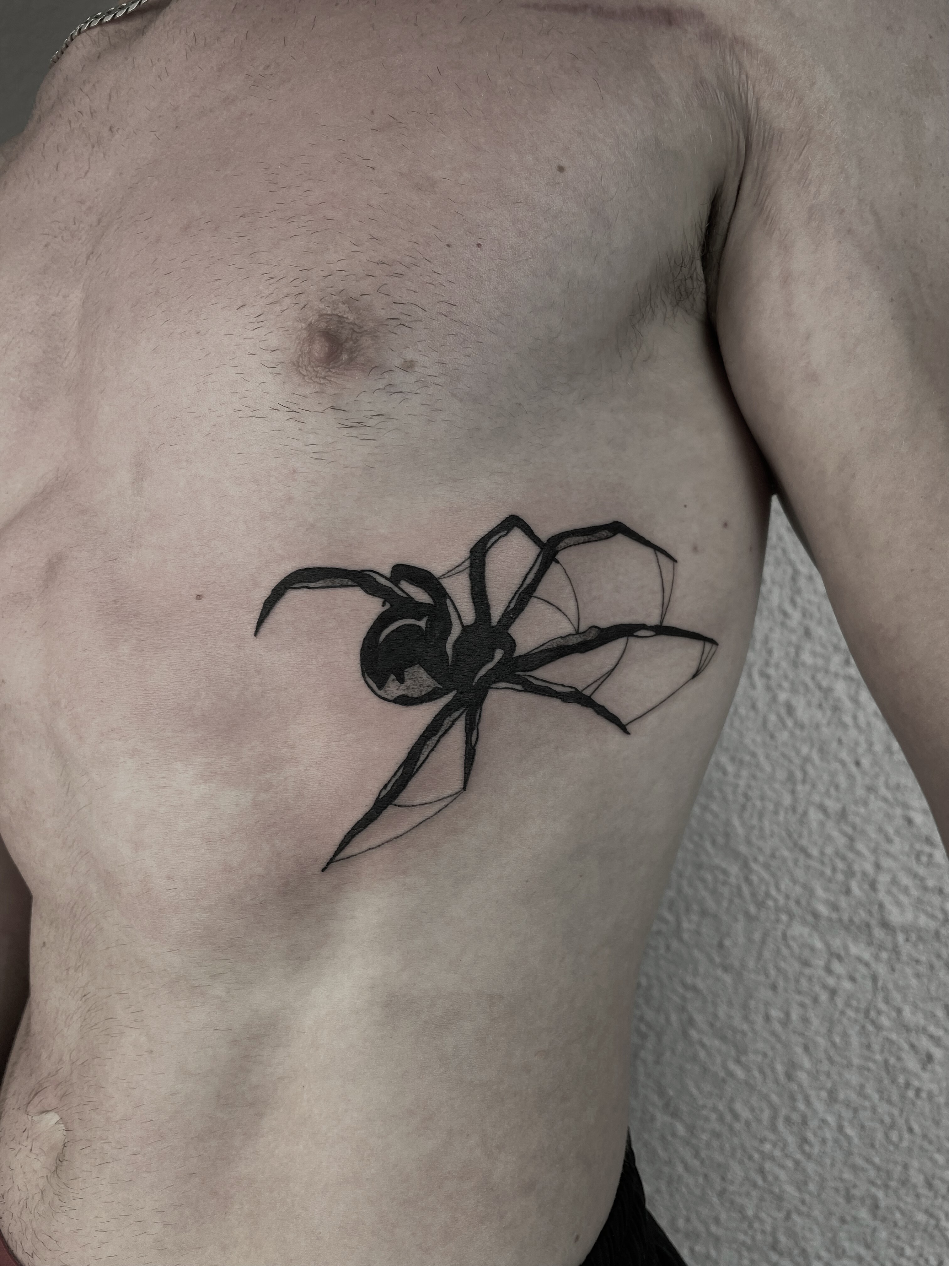 black spider tattoo on the chest in bold blackwork style